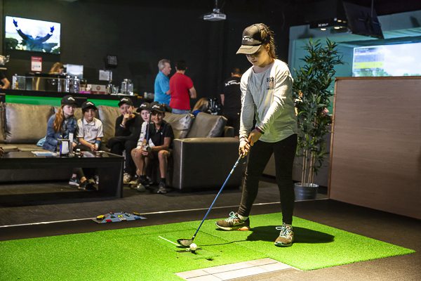 Young golfer practicing swing on simulator green at X-Golf