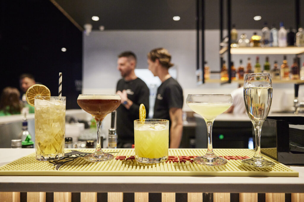 Cocktails lined up at X-Golf bar with staff and guests behind
