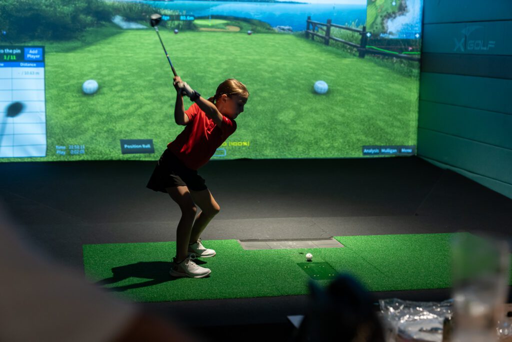 Young girl swinging golf club at X-Golf indoor simulator setup