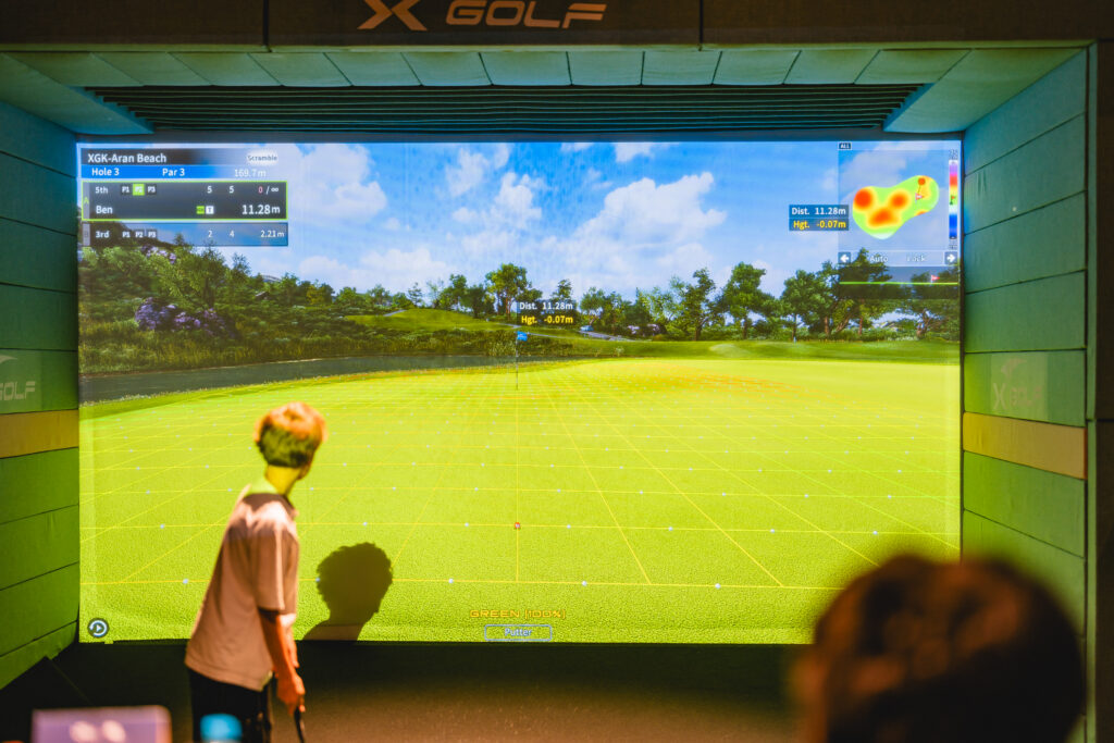 Child playing golf on X-Golf simulator screen in indoor bay