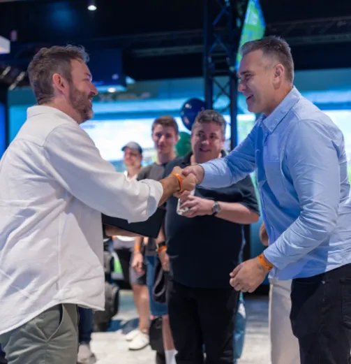 Two business partners smiling and shaking hands inside an X-Golf venue to celebrate a syndicate partnership.