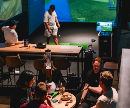 Friends socialising beside simulator bays at X-Golf Surrey Hills